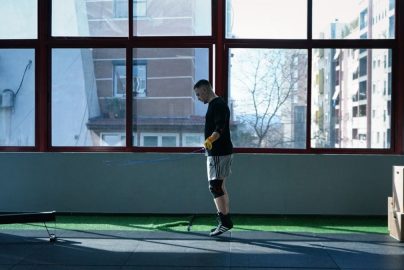 Young man exercising with a skipping rope in an urban gym with large windows and city view.